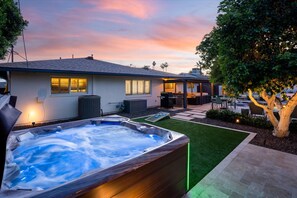 A residential setting with a hot tub, a patio area, and a house with a covered outdoor seating area. - Elevated Old Town Scottsdale Pool| Spa| Sauna|Gym (Scottsdale)