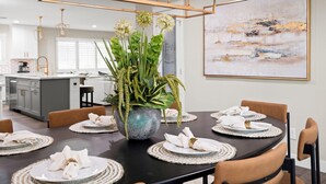 A dining area with a round table set for six, surrounded by chairs. A large potted plant with green foliage is placed in the center. - Elevated Old Town Scottsdale Pool| Spa| Sauna|Gym (Scottsdale)