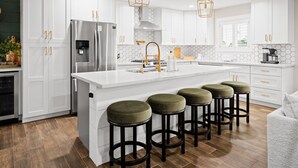 A modern kitchen with white cabinets, a stainless steel refrigerator, a large island with stools, and pendant lighting. - Elevated Old Town Scottsdale Pool| Spa| Sauna|Gym (Scottsdale)
