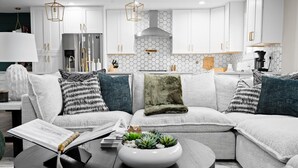A modern living room with a sectional sofa, a coffee table with a succulent centerpiece, and a kitchen in the background with white cabinets and a hexagonal backsplash. - Elevated Old Town Scottsdale Pool| Spa| Sauna|Gym (Scottsdale)
