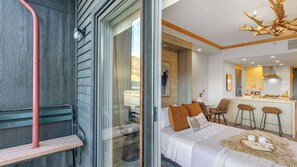 Ein modernes Hotelzimmer mit Bett, einer Sitzgruppe mit einer Bank, einem Essbereich mit Barhocker und einer Küche mit Kochinsel.