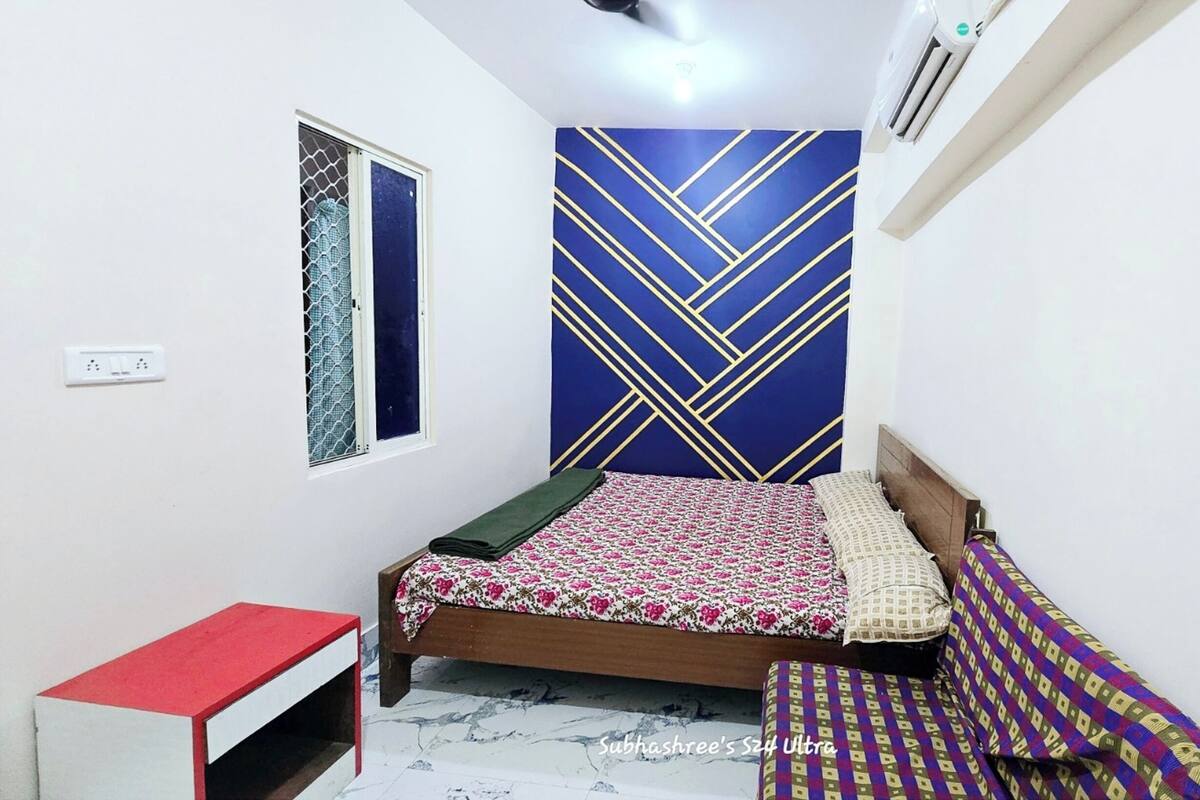 A bedroom with a bed, a bedside table, a window with a decorative screen, and a wall-mounted air conditioner.