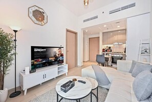Ein modernes Wohnzimmer mit einem Flachbildfernseher, einem weißen Sofa, einem Couchtisch und einer Küche im Hintergrund.