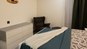 Ein Schlafzimmer mit einem Bett, einem Sessel, einer Kommode und einem an der Wand befestigten Regal mit einem Bild.