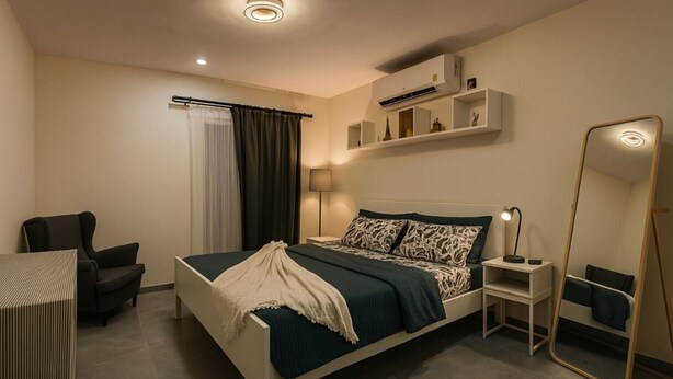 Ein modernes Hotelzimmer mit Bett, Schreibtisch, Stuhl, Nachttisch, Lampe, Spiegel und Klimaanlage.