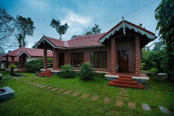 A brick house with a red-tiled roof, surrounded by a well-maintained garden with stepping stones leading to the entrance. - Coffee County Homestay (Srimangla)