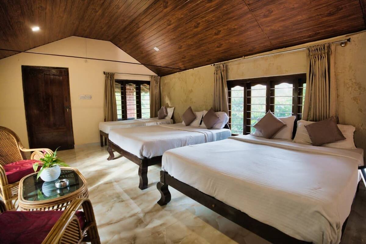 A room with three beds, a wooden ceiling, and a view of greenery outside.