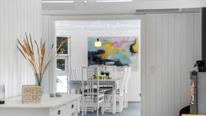 Un interior moderno con comedor, mobiliario blanco, chimenea y un cuadro abstracto colorido.