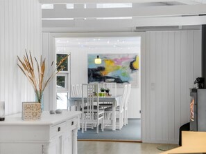 Ein modernes Interieur mit Essbereich, weißen Möbeln, einem Kamin und einem farbenfrohen abstrakten Gemälde.
