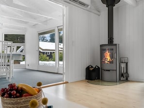 Ein Zimmer mit Kaminofen, einem Esstisch mit Obst und Blick auf eine verschneite Landschaft durch Glastüren.