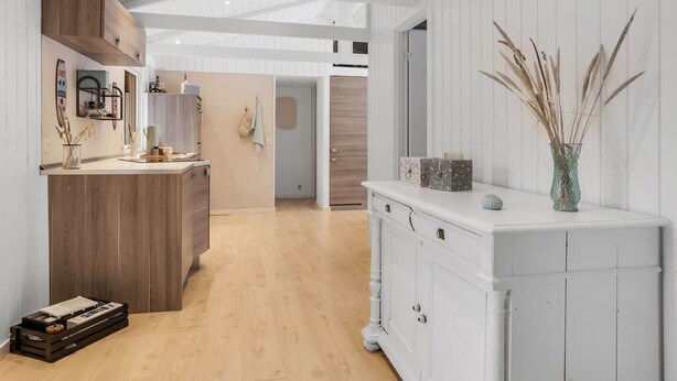 Un pasillo amplio con suelo de madera, paredes blancas y un armario blanco con objetos decorativos.