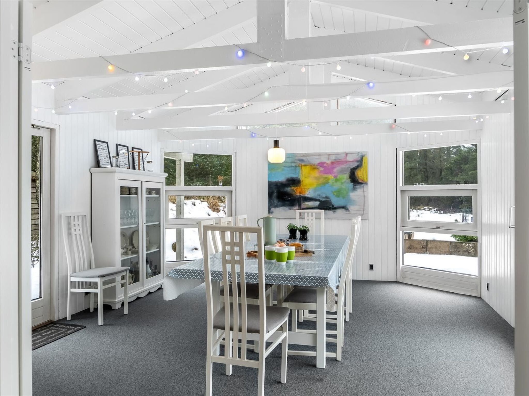 A dining area with a table, chairs, and a view of a snowy landscape through large windows.