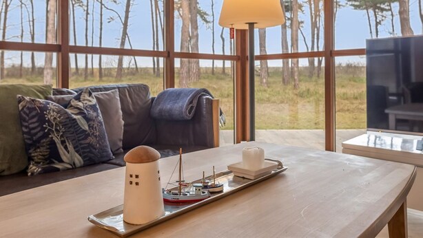 Ein Zimmer mit einem großen Fenster, einem Sofa mit gemusterten Kissen, einem Holztisch mit einem Schiffmodell und einer Lampe.