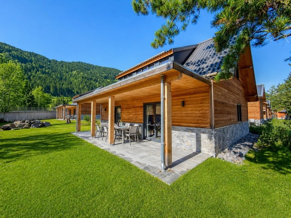 A modern wooden house with a covered patio and stone foundation.