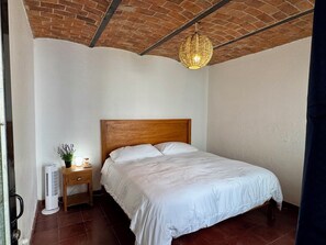 A bedroom with a wooden headboard, white bedding, a bedside table with a lamp, and a hanging light fixture. - Central Ajijic 3-Bedroom House, Near Everything! (Ajijic)