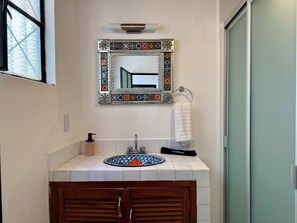 Une salle de bain avec un lavabo carrelé, un miroir orné de motifs décoratifs, un porte-serviettes et un meuble en bois.