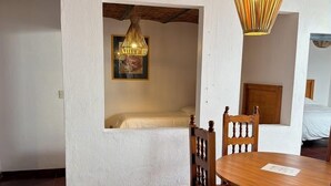 Ein Zimmer mit einem Bett, einem Esstisch mit Stühlen, einer Hängelampe und einer Ziegeldecke.