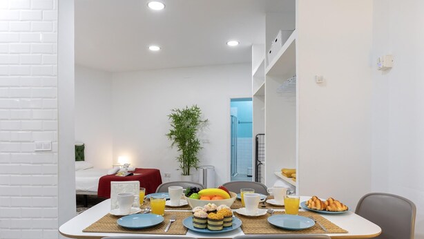 Un espace repas moderne avec un mur en briques blanches, une table à manger dressée avec des assiettes, des tasses et un saladier rempli de fruits.