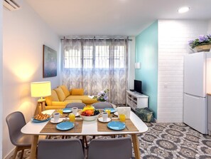 Ein kompakter Wohnbereich mit Essplatz, Sofa, Fernseher und Kühlschrank.