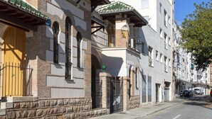 Une vue de rue d’un immeuble à la façade traditionnelle, caractérisée par un socle en pierre, des fenêtres en arc de cercle et un toit recouvert de tuiles vertes.
