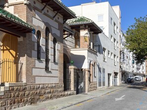 Blick auf eine Straße mit einem Gebäude, das eine traditionelle Fassade hat, mit einer Steinsockel, Rundbogenfenstern und einem grünen Ziegeldach.