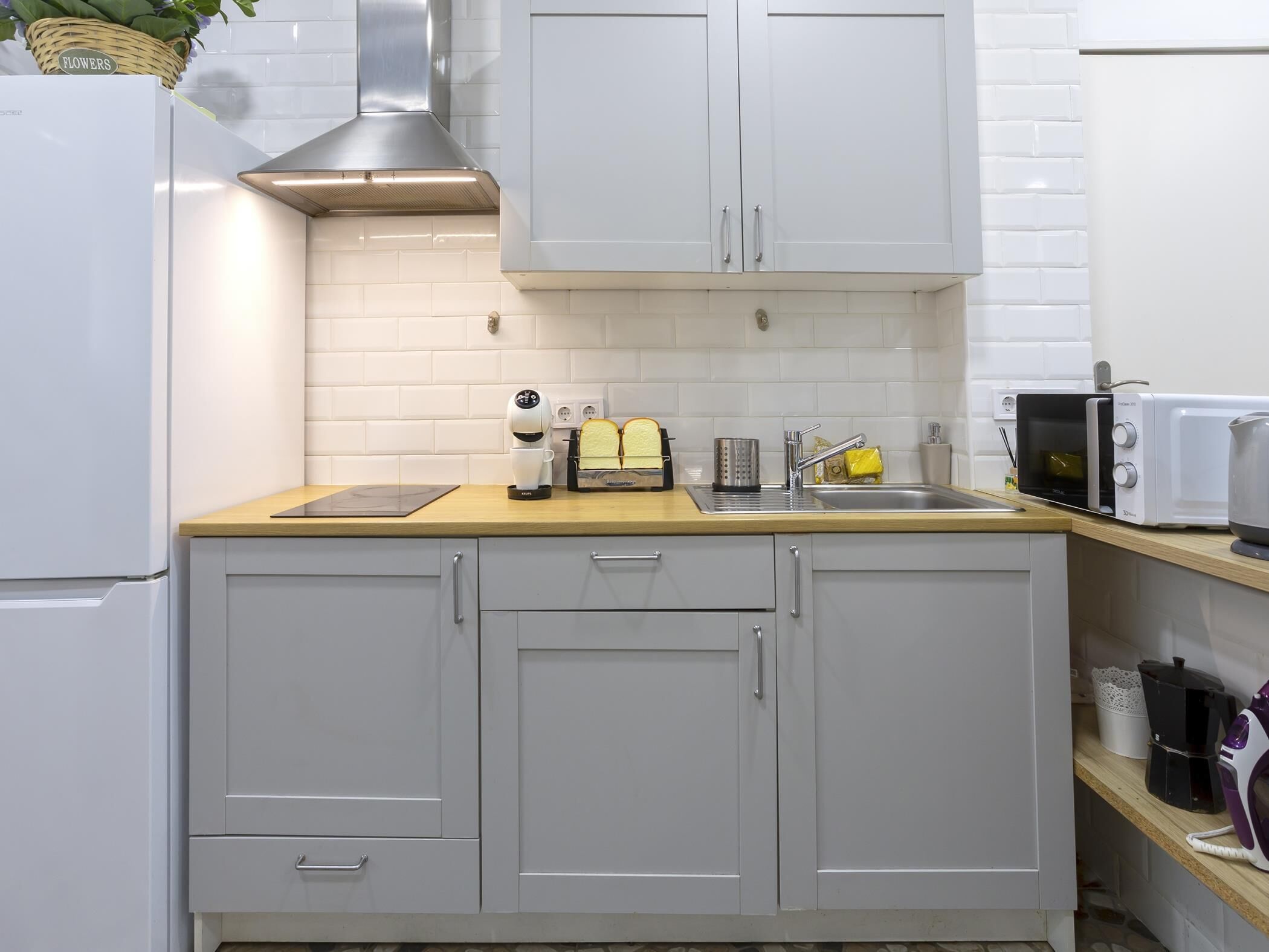 A compact kitchen with white cabinets, a stainless steel range hood, a toaster, a microwave, and a coffee maker.