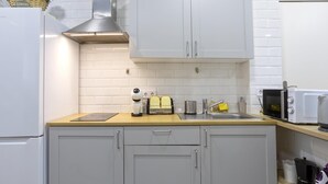 Une cuisine compacte avec des meubles blancs, une hotte en acier inoxydable, un grille-pain, un four à micro-ondes et une machine à café.