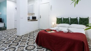 Une chambre d’hôtel avec un lit, une table de chevet, un miroir, une porte et un sol carrelé.