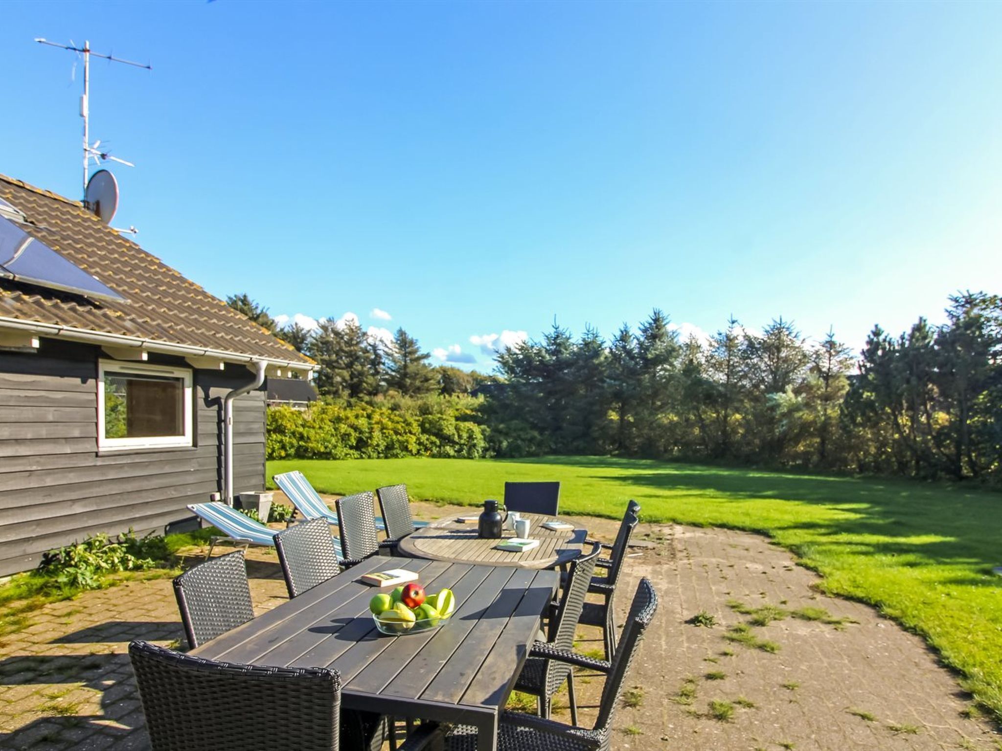 A patio with a table and chairs, a hammock, and a view of a green field and trees.