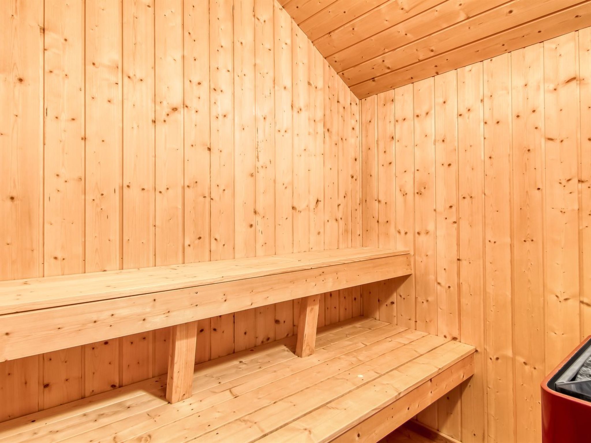 A wooden sauna with benches and a red container.
