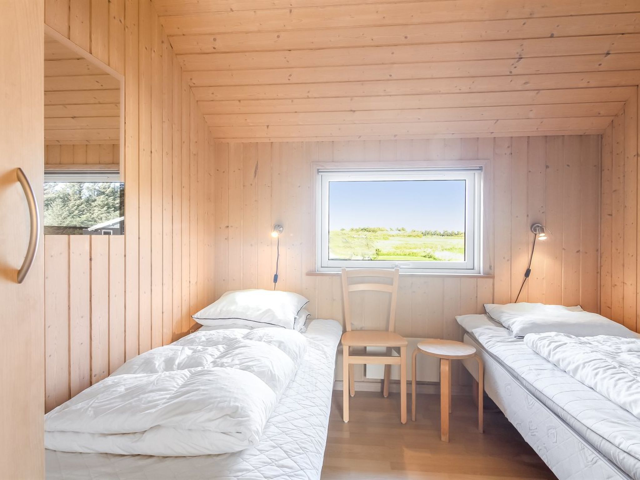 Una habitación pequeña y acogedora con dos camas, una silla y una ventana que ofrece vistas al exterior.