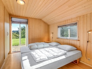 Una habitación con paneles de madera, una cama, un ventanal y una puerta que da a un balcón.