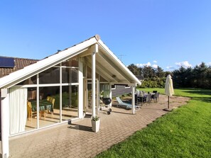 Un patio cubierto con cerramiento de vidrio, mobiliario exterior y césped.