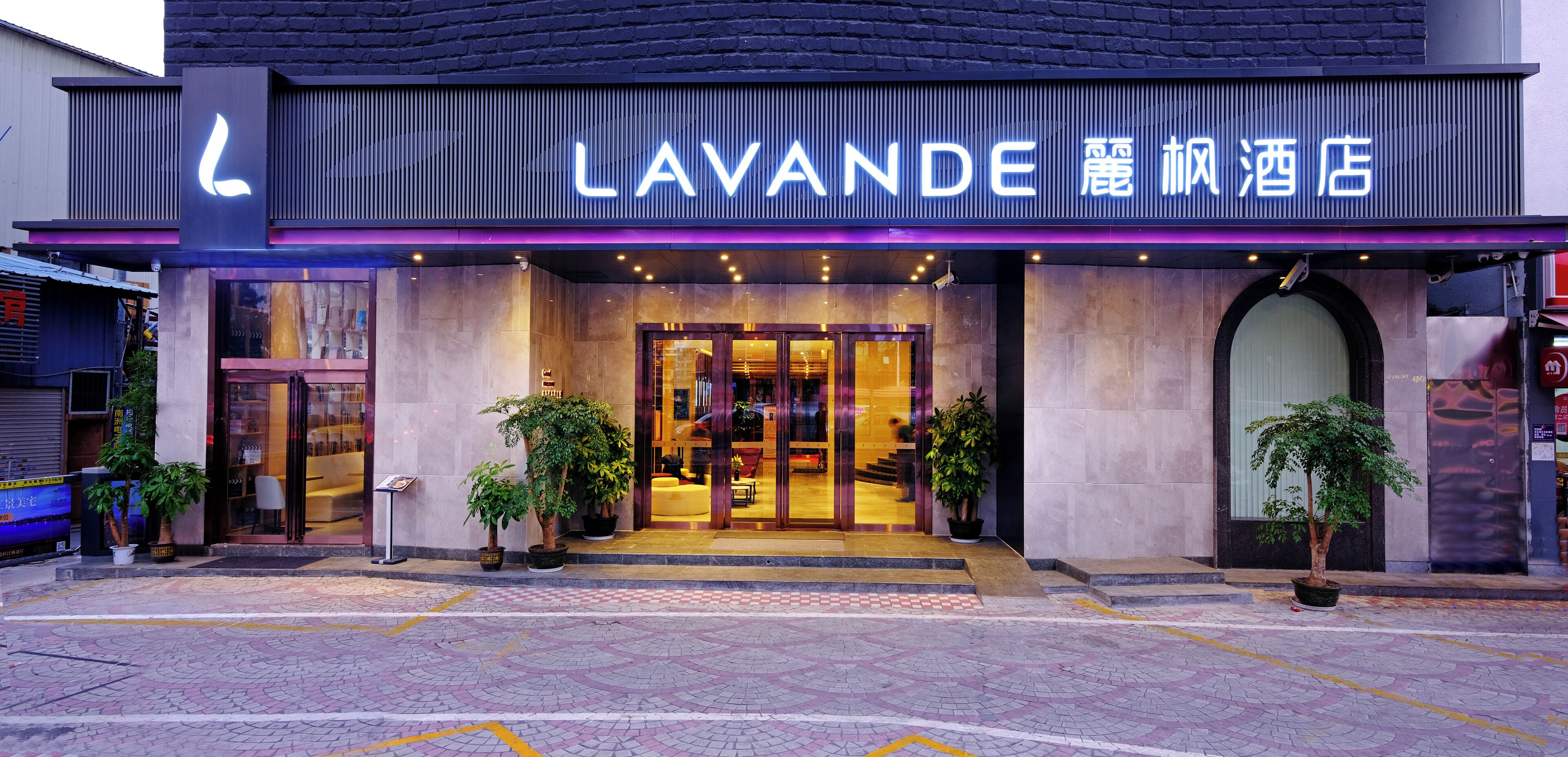 Ingresso di un hotel con un cartello ben visibile con la scritta "LAVANDE" e caratteri cinesi. All'ingresso ci sono piante in vaso e la facciata presenta una combinazione di vetro e pietra.