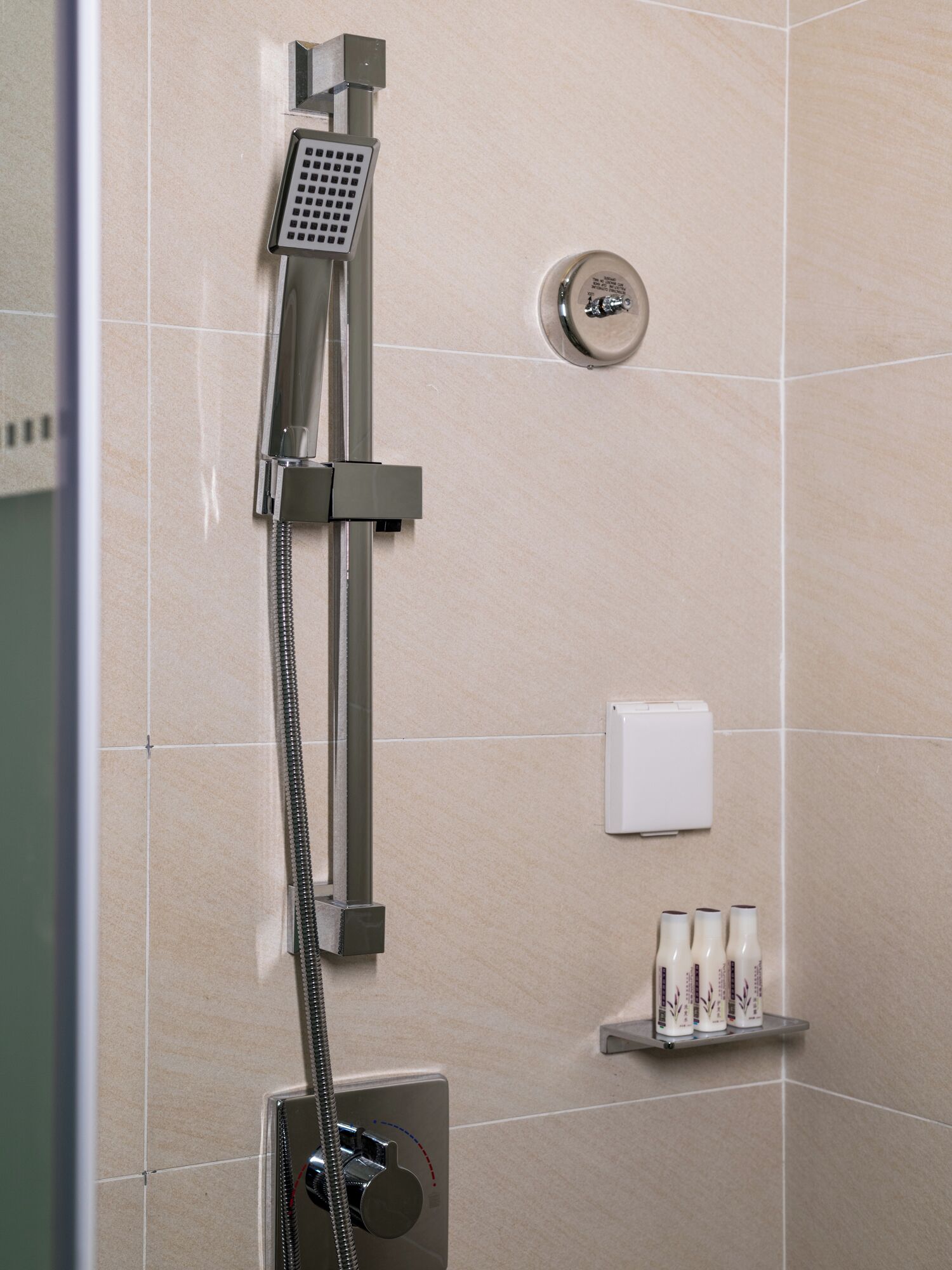 Una ducha con cabezal de ducha de mano y panel de control en la pared.