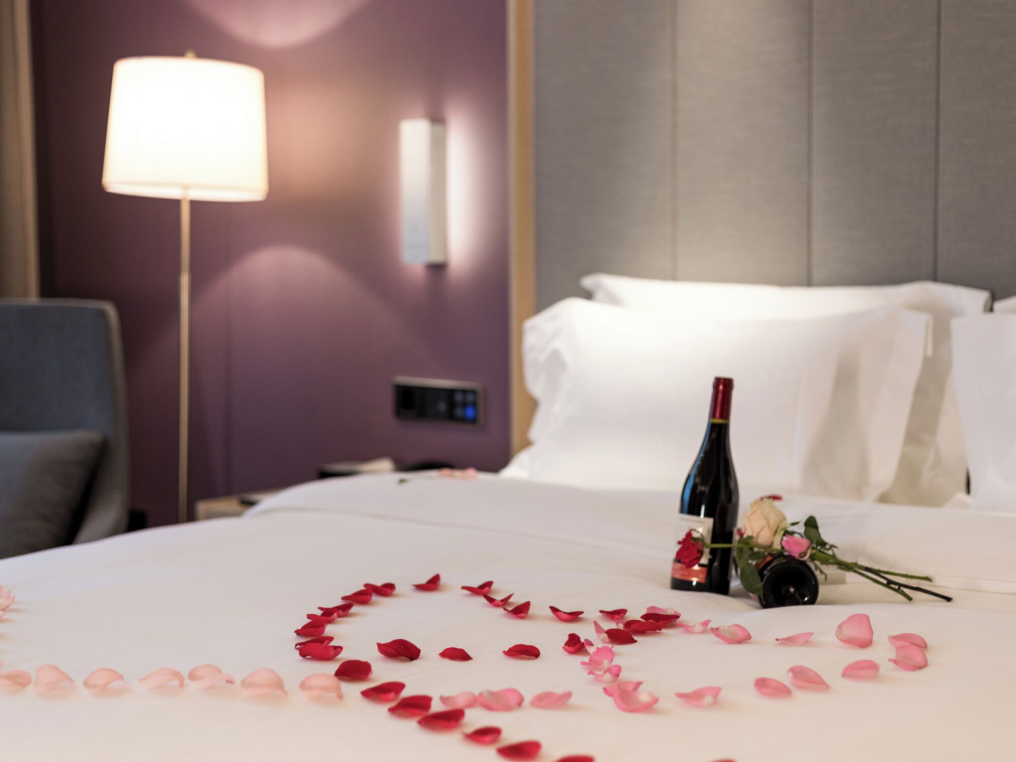 A hotel room with a bed, a bedside table, a lamp, and a bottle of wine.