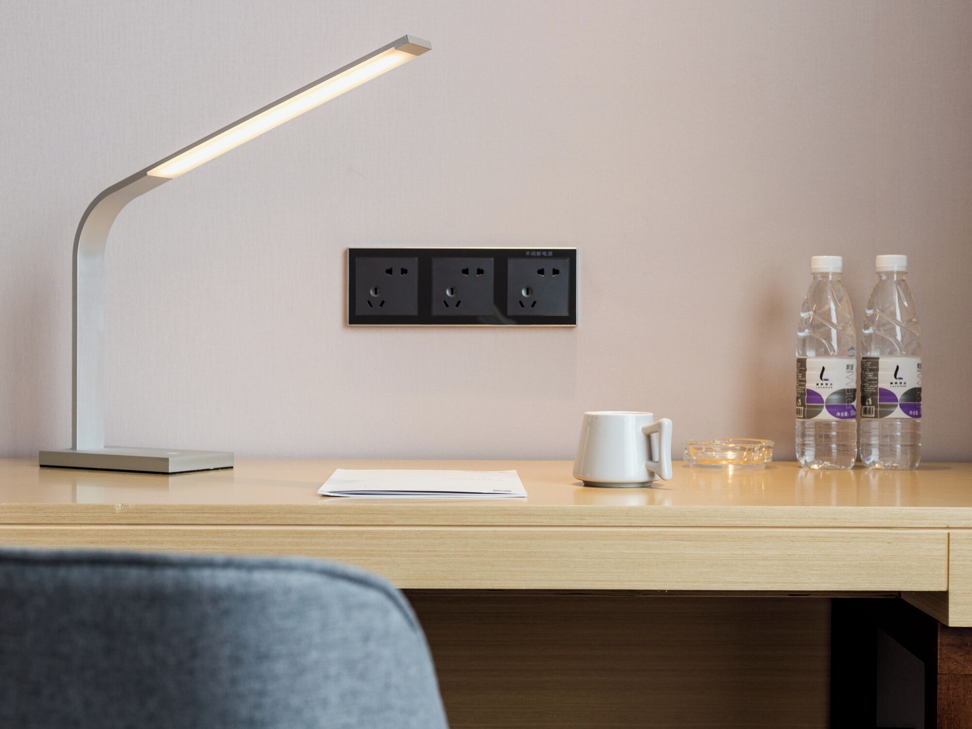 A desk with a desk lamp, two bottles of water, a mug, and a power outlet.