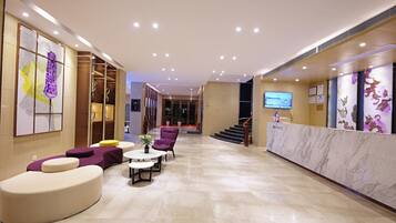 Un moderno vestíbulo de hotel con mostrador de recepción, zona de estar y una escalera que lleva a otras plantas.