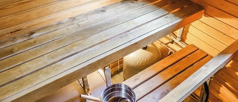 Una sauna con bancos de madera y un recipiente metálico.