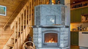 A stone fireplace with a fire, a wooden staircase, and a kitchen area with green cabinets.