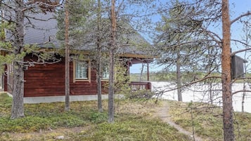 Een houten chalet met een veranda, omgeven door bomen en een heldere lucht.