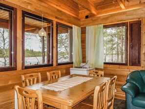 A wooden cabin interior with a dining table, chairs, a radio, and large windows.