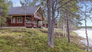 Une cabane en bois avec un porche, entourée d’arbres et d’une zone herbeuse.
