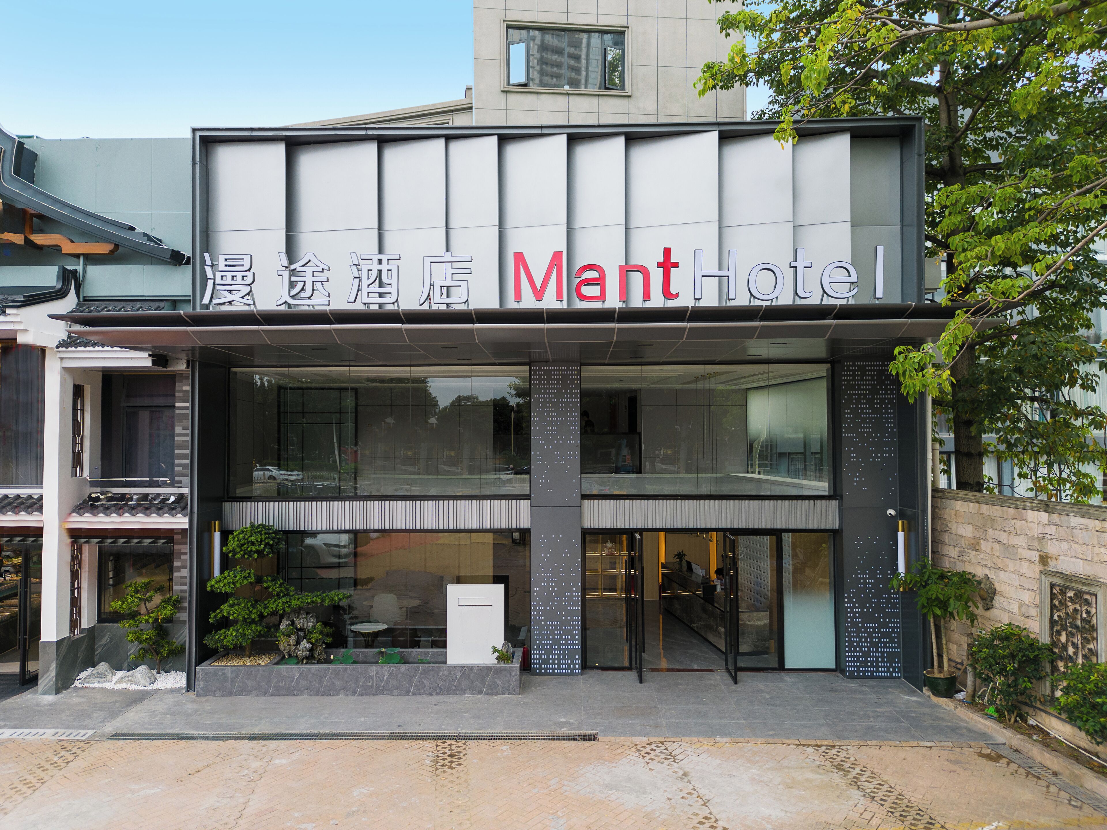 Un hotel con fachada moderna, amplios ventanales de vidrio y un letrero que dice "Mant Hotel".