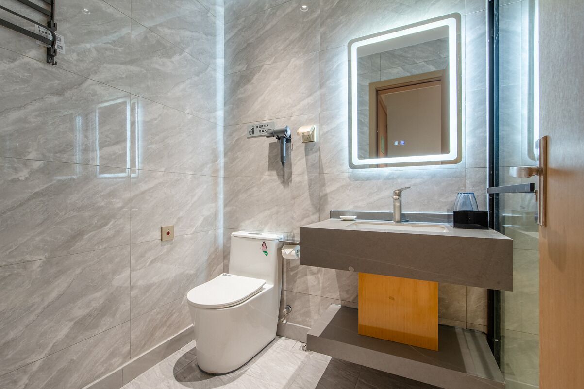 A modern bathroom with a marble wall, a toilet, a sink with a mirror, and a shower area.