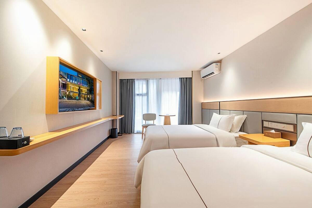 Une chambre d’hôtel avec deux lits, un téléviseur fixé au mur, une petite table et une chaise.
