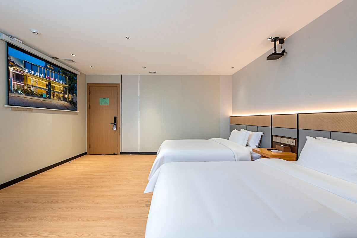 Habitación de hotel con dos camas, piso de madera, un cuadro en la pared y una puerta con un cartel.