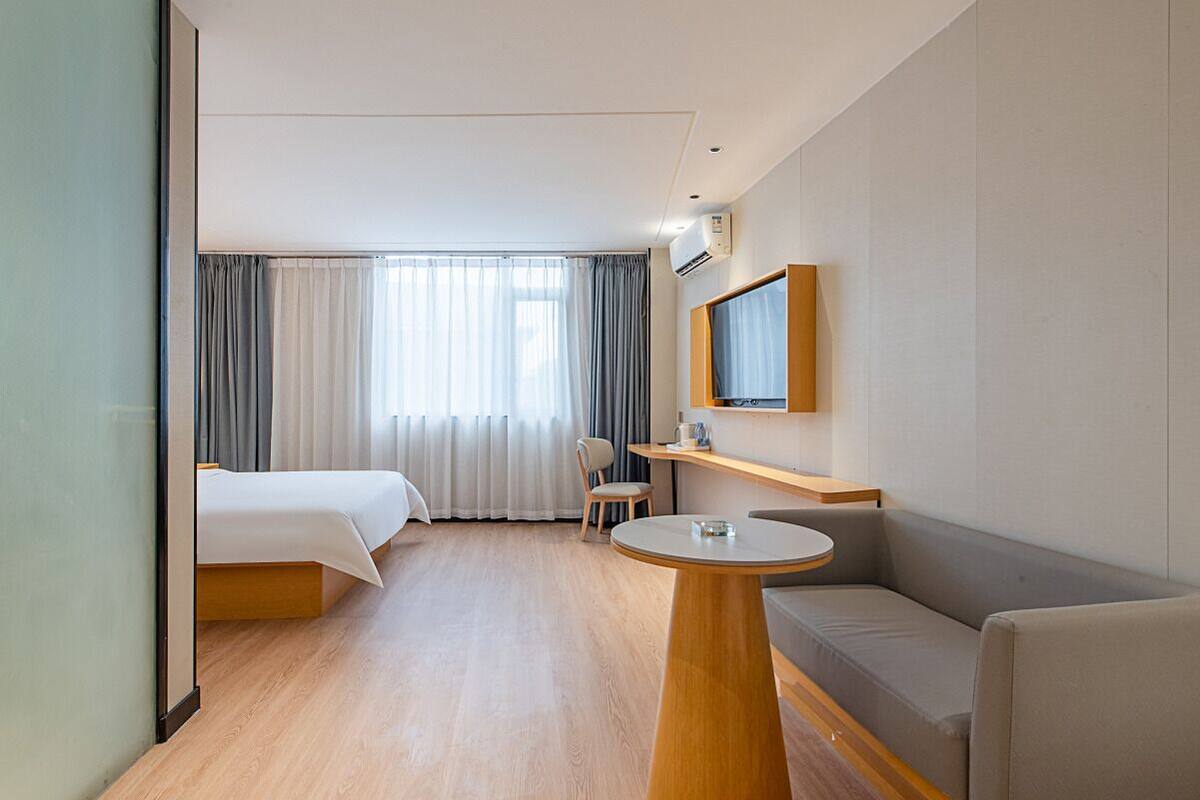 Une chambre d’hôtel avec deux lits, un canapé, une petite table, une télévision et une fenêtre avec des rideaux.