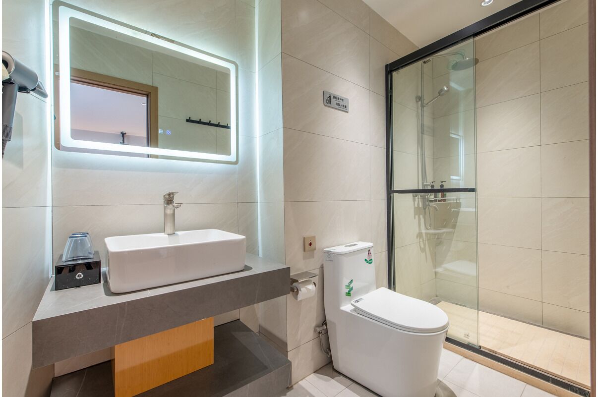 A modern bathroom with a large mirror, a sink, a toilet, and a glass-enclosed shower area.