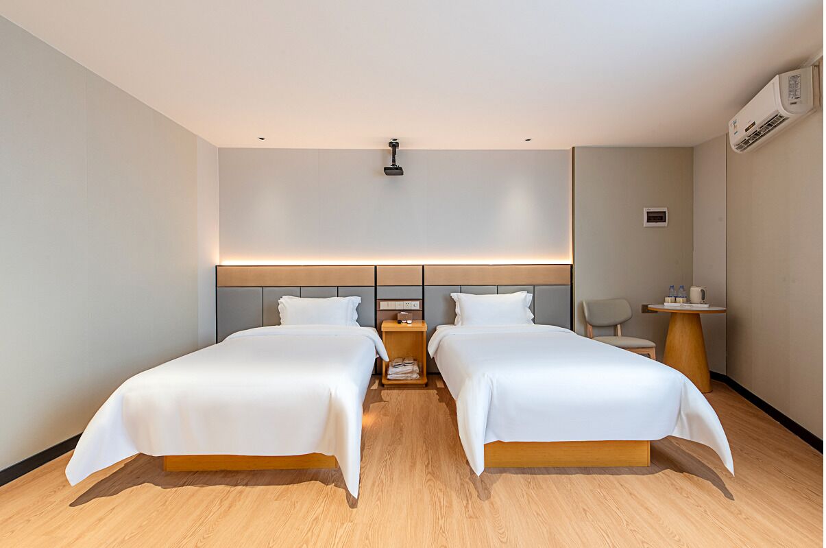 Habitación de hotel con dos camas, una mesita de noche con lámpara, una silla y un equipo de aire acondicionado.